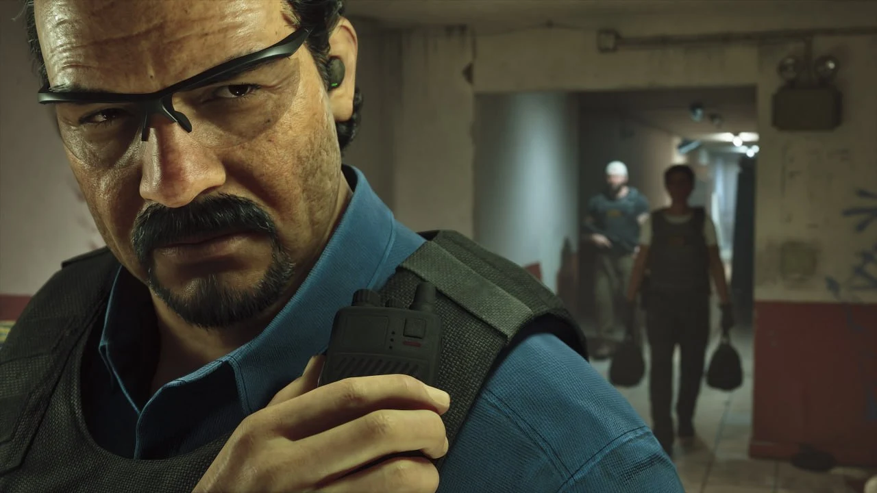 GTA 6 screenshot from Edge — a man with a moustache and glasses in a tactical vest speaking into a radio in a corridor, armed people behind him