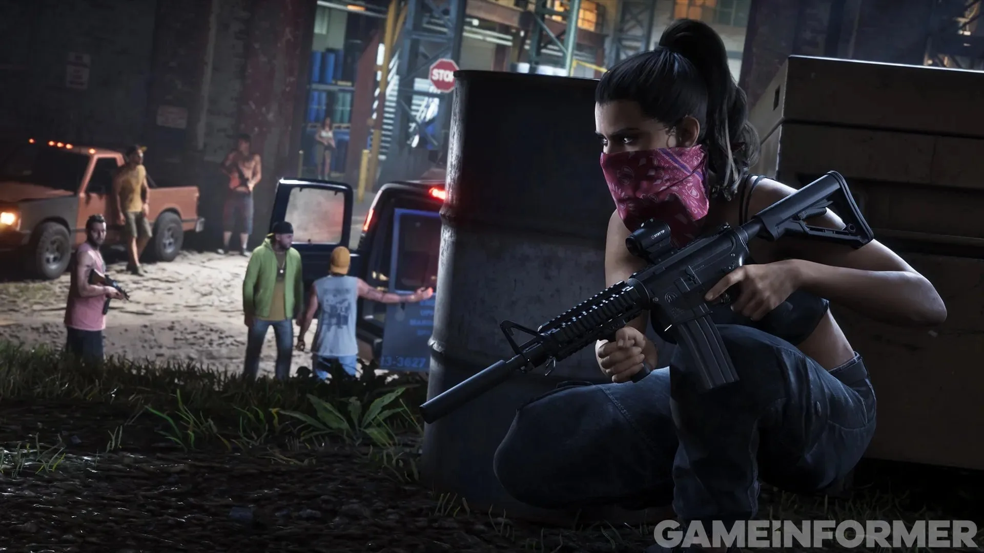 GTA 6 screenshot from Game Informer — Lucia in a bandana crouching behind a barrel with a suppressed rifle, armed men by a truck behind her