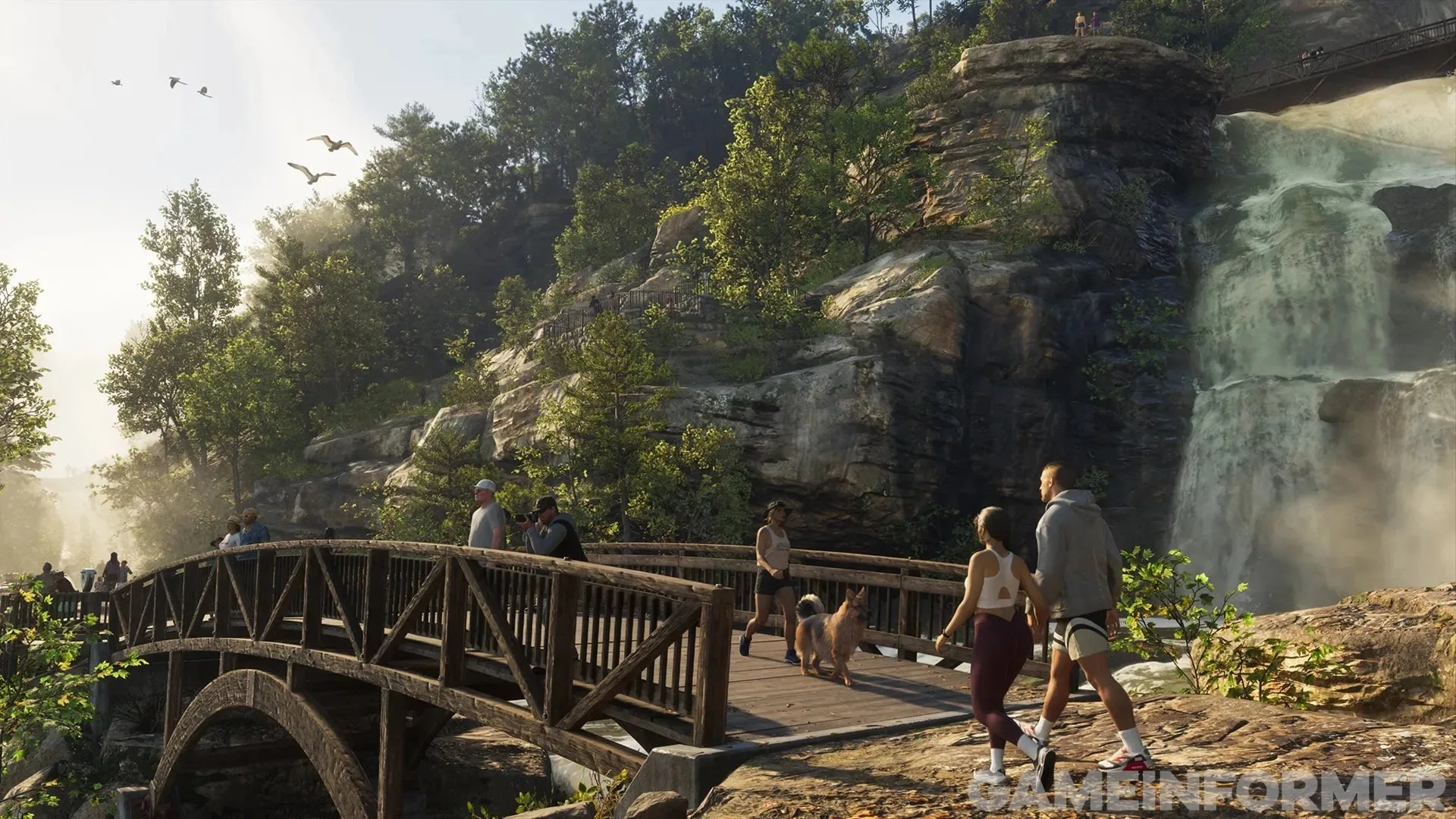 GTA 6 screenshot from Game Informer — hikers and a runner with a dog on a wooden footbridge below a waterfall