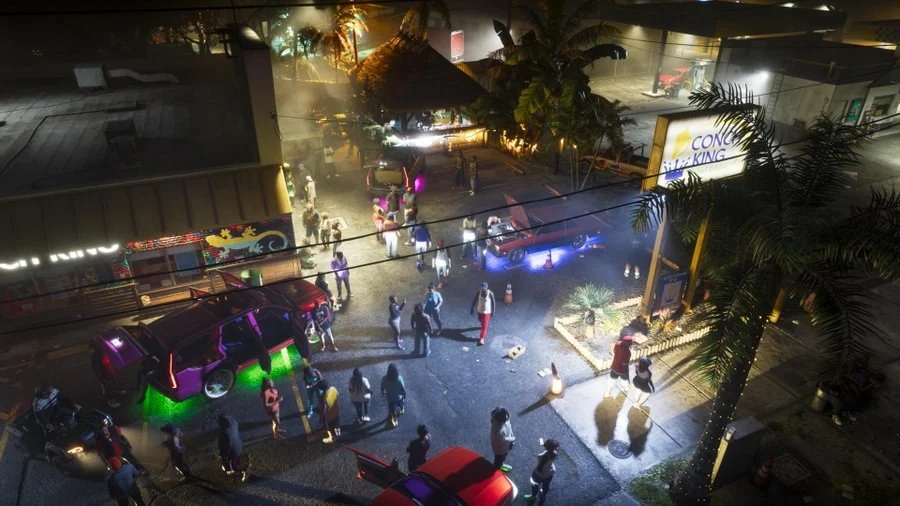 Official GTA 6 screenshot: a crowded street at night with parked cars and neon signs (released October 8, 2026)