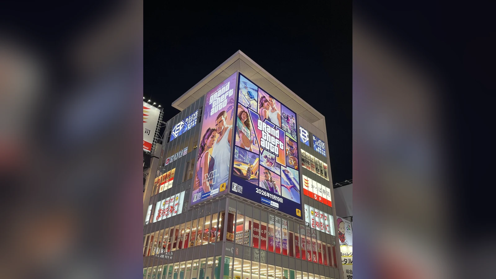 GTA 6 billboards wrapped around the corner of a building in Osaka at night: Jason and Lucia on one side, a collage of official artwork with the logo and 2026年11月19日 on the other