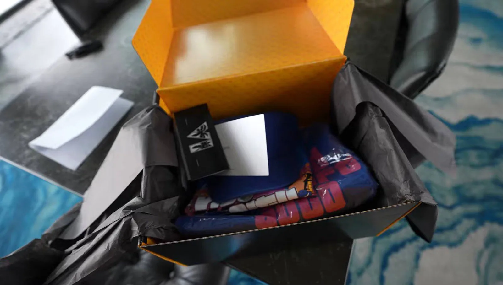 Opened Rockstar merch box, orange inside, with folded blue merch, a black card and a note in black tissue paper (creator's photo)