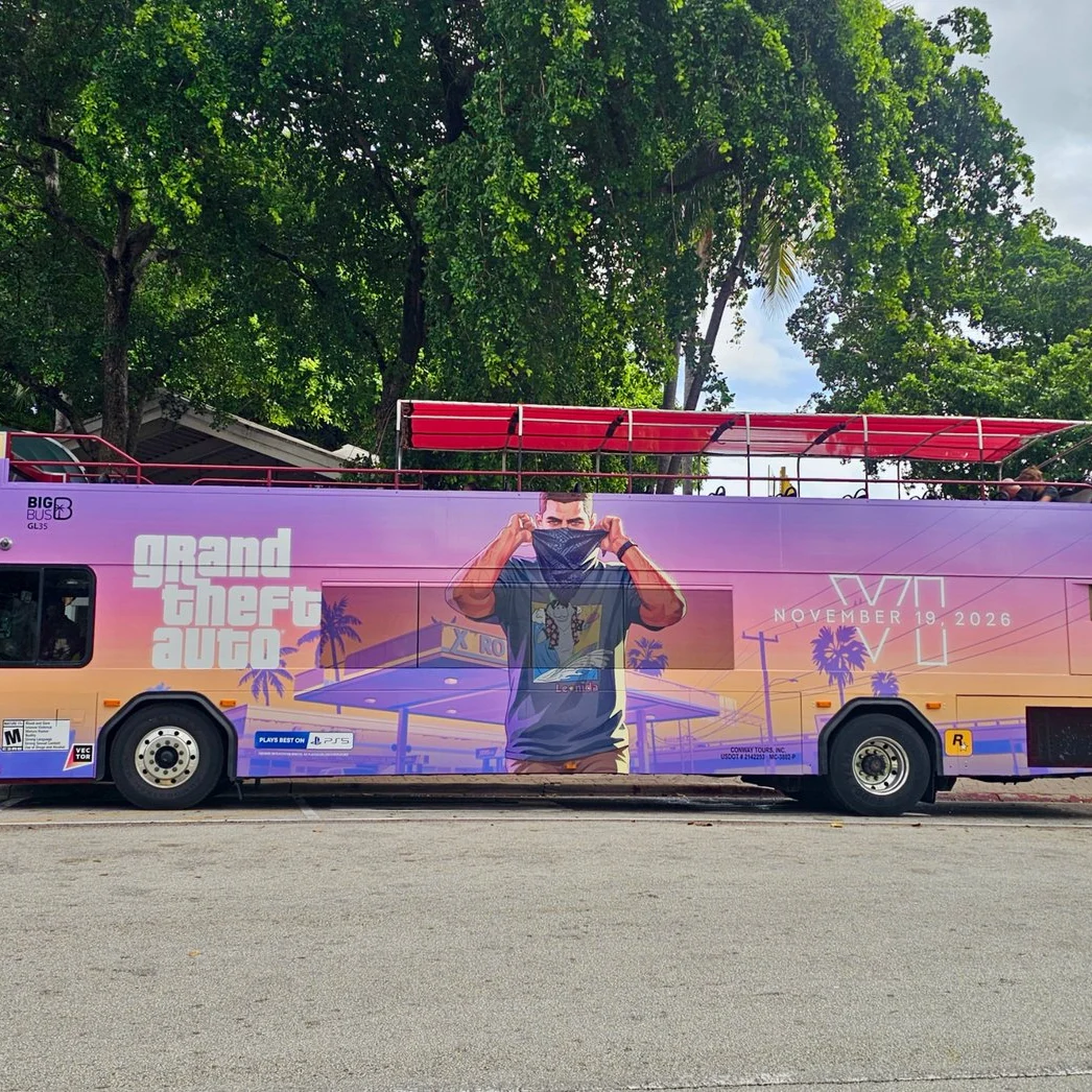 Open-top double-decker sightseeing bus in Miami wrapped in GTA 6 art: Jason pulling up a bandana at a Xero gas station, the logo and November 19, 2026