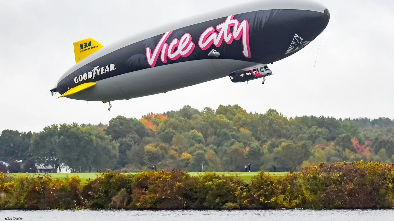 Goodyear blimp Wingfoot Three (N3A) in a black GTA 6 Vice City livery flying low over a lake (photo: RA Durfee)